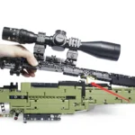 A hand holds a black scope attached to a green and black brick toy gun.