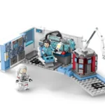 Two toy figures are present, one seated at a control panel, and the other standing with a helmet.