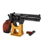 A toy gun with black and brown elements rests on a yellow stand, with two additional brick pieces nearby.