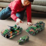 A child plays with three toy military vehicles, including a tank, an armored car, and a jeep.