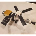 A toy satellite with black solar panels and a gold rectangular section.