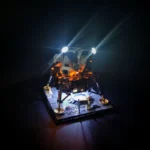 A toy lunar lander with lights is on a black base.