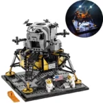 A toy lunar lander with two astronaut figures and an American flag on a gray base.