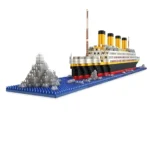 A toy ship with yellow funnels and a red and black hull sits on a blue base next to a gray iceberg.