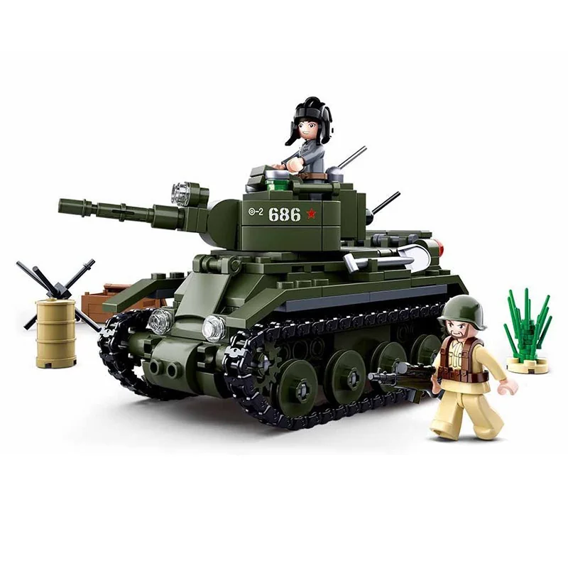A green toy tank with two toy figures, a barrel, and some grass is visible.