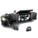 A black toy truck with an opened side panel, revealing a control room with screens, and three small barriers.